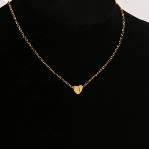 Vista detallada de un colgante de corazón dorado con la letra D en un soporte de terciopelo