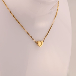 Detalle de un colgante de corazón de acero inoxidable dorado con la letra U grabada