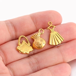 Détails de trois pendentifs dorés en forme de sac et robe présentés dans une main