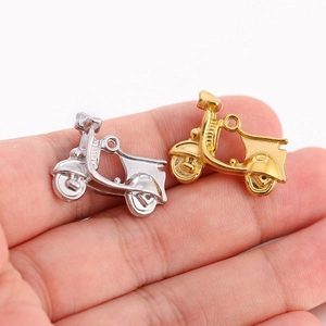 Détails macro des pendentifs scooter en or et argent tenus à la main pour la taille