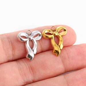 Pendentifs nœuds en acier poli doré et argenté tenus en main pour l'échelle