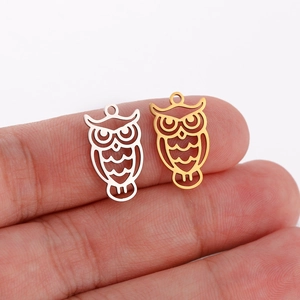 Detail view of owl charms in gold and silver, showing size reference on fingertips