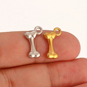 Macro view of mini bone charms in gold and silver finish on a fingertip for size reference