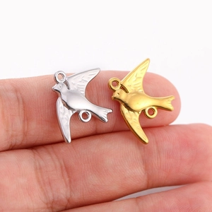 Détail macro de pendentifs en forme d'oiseau en or et argent posés sur un doigt