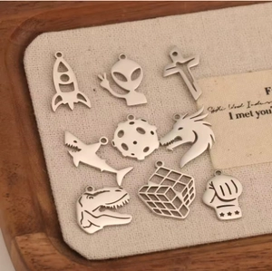 Assorted stainless steel charms featuring rocket, alien, and dinosaur icons on a tray