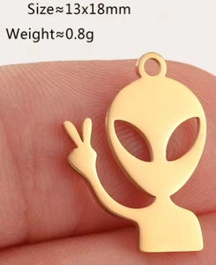 Macro view of golden alien peace sign pendant on fingertip showing 13x18mm size