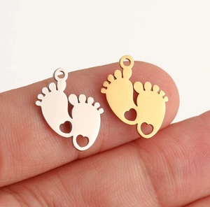 Polished tiny stainless steel baby footprint pendants in gold and silver held by hand