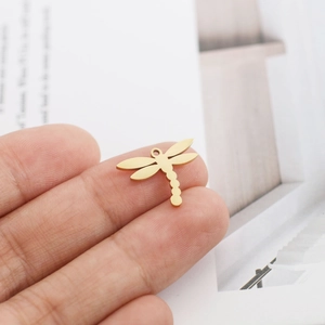 Vue macro d'un petit pendentif libellule doré sur un doigt montrant la taille miniature