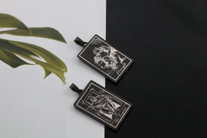 Détail de pendentifs tarot noirs montrant la Force et l'Empereur gravés sur de l'acier