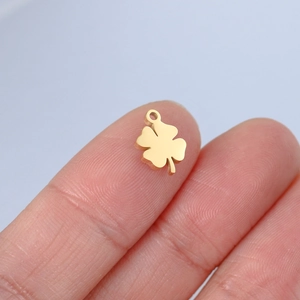 Minimalistischer matter Gold-Kleeblattanhänger für DIY-Schmuck auf einer Fingerspitze