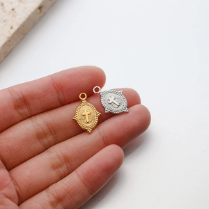 Close-up of gold and silver stainless steel oval cross pendants with sunburst relief detail