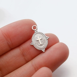 Macro shot of a vintage oval cross pendant in silver finish held by fingers for scale