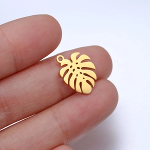 Macro detail of a polished golden monstera leaf pendant held between fingers for size
