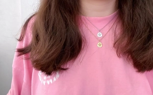 Close-up of layered stainless steel necklaces with engraved floral pendant on female neck
