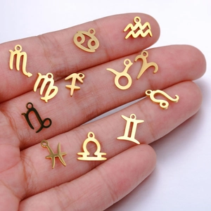 Macro shot of twelve golden zodiac charms held by hand for DIY jewelry making size scale
