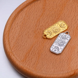 Macro detail of sun and moon engraved steel rectangle charms in gold and silver