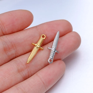Detail of small gold and silver sword pendants held in palm showing size and texture