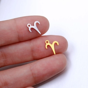 Macro view of Aries zodiac charms in gold and silver showing precise size on a finger