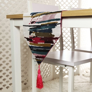Detail of colorful striped table runner with vibrant rose red silk tassel on wood surface