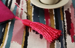 Detail of rose red tassel pendant on a colorful striped jacquard fabric table runner