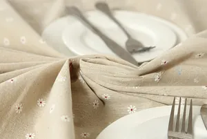 Close-up of linen tablecloth with daisy floral print, white plates and stainless cutlery