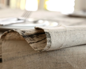 Macro shot of rustic linen tablecloth featuring natural wood grain texture and fine sewing