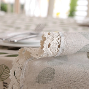 Detailed close-up of pastoral green leaf tablecloth with vintage lace edge and linen texture