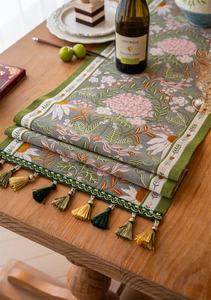 Detail of floral jacquard table runner featuring green fringe and tassel accents