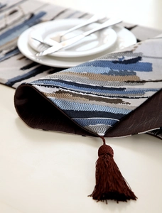 Detail of jacquard table runner featuring abstract blue stripes and brown fringe tassels