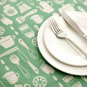 Close-up of light green linen tablecloth with white kitchen icons and cutlery detail