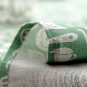 Macro shot of cotton linen tablecloth showing green kitchenware print and fine stitching
