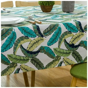 Thick cotton tablecloth with green tropical leaf patterns on a wooden dining table