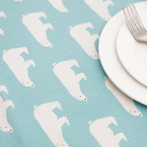 Close-up of linen-textured tablecloth with cute white polar bear pattern on light blue fabric