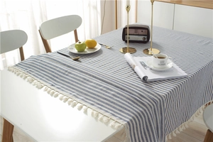 Detail view of blue and white striped cotton tablecloth with cream fringe tassels