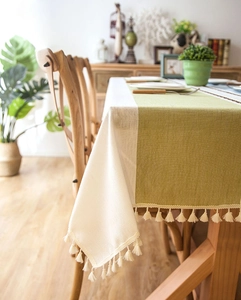Detail of sage green and beige tablecloth with linen texture and cotton fringe