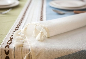 Detailed close-up of geometric embroidered table runner with white cotton tassels