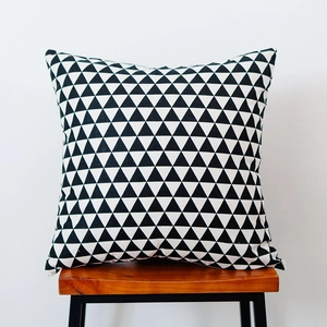 Detail of a square black and white triangle pattern cushion on a wooden stool