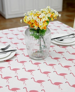 Detail of flamingo print tablecloth with a floral vase and elegant tableware setting