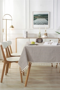 Detail of grey striped tablecloth featuring white tassel pom-poms on a wooden dining table