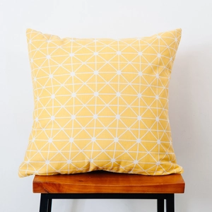 Detail of yellow geometric pillow with white grid pattern on a wooden stool
