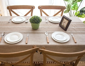 Close-up of linen tablecloth featuring white lace bands and delicate tassel ball edges