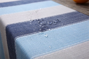 Close-up of waterproof fabric showing water droplets on blue striped linen tablecloth