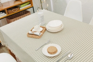 Detail of green striped cotton tablecloth featuring delicate white fringe tassels and soft texture