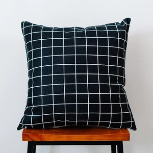 Detail of Nordic black and white plaid square pillowcase on a rustic wooden stool