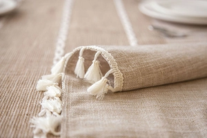 Detail of beige linen table runner with white hollow lace and tassel fringe decoration
