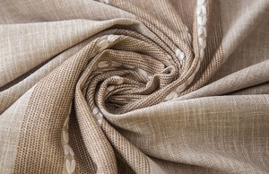 Macro shot of beige linen tablecloth featuring white geometric embroidery and tassels