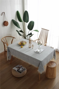 Detail of gray checkered linen tablecloth with decorative white fringe on a wooden table