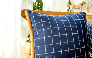 Detail of navy blue plaid cushion cover with geometric fringe trim on wooden chair