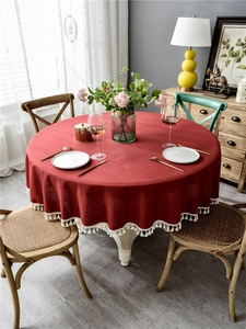 Close-up of red round tablecloth with cream fringe tassels on a vintage wooden table