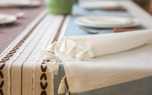Close-up of geometric embroidered pattern and white tassels on cotton linen tablecloth